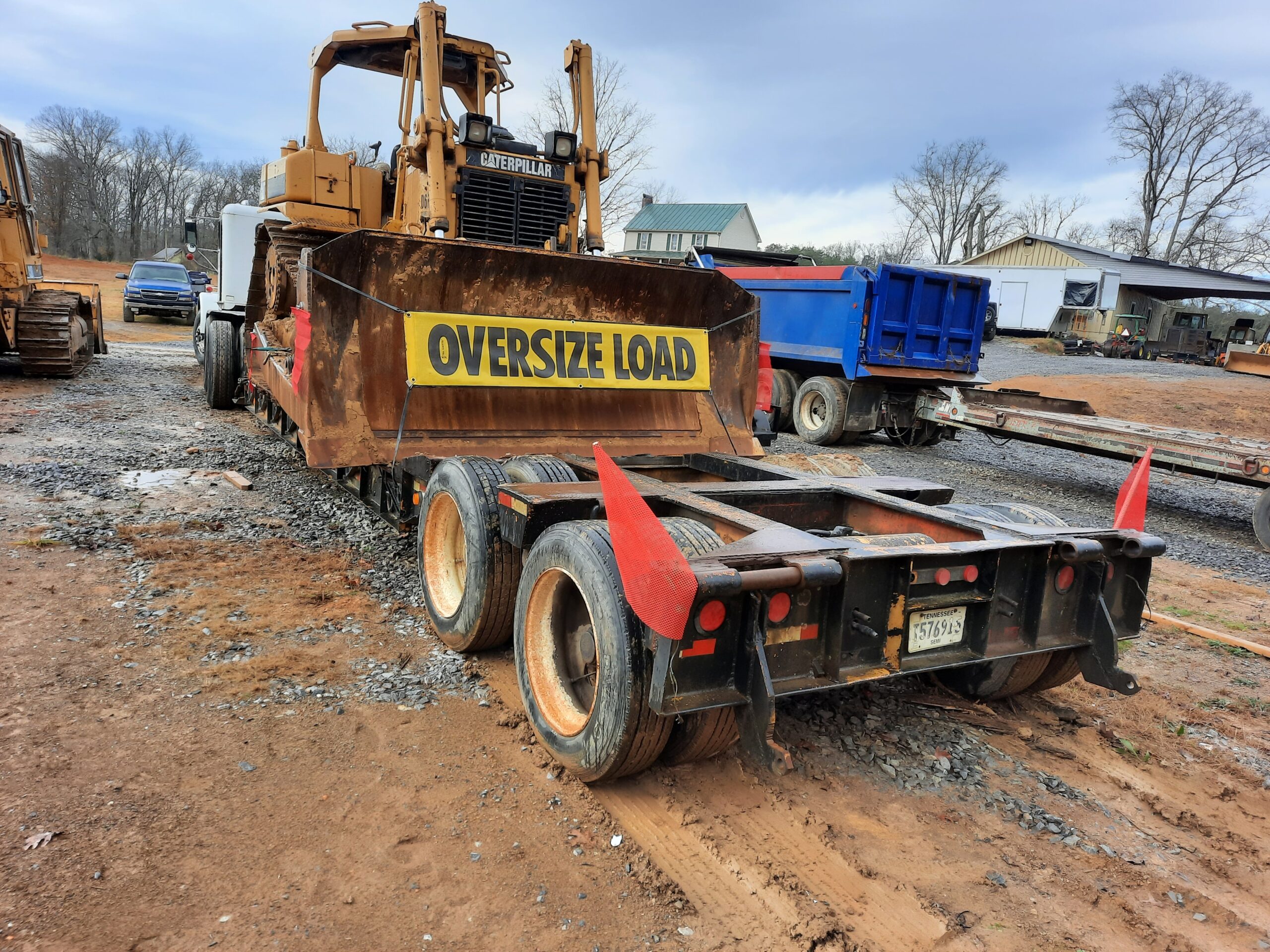 grommet oversize load banner on bulldozer with staff flags on trailer at a construction site