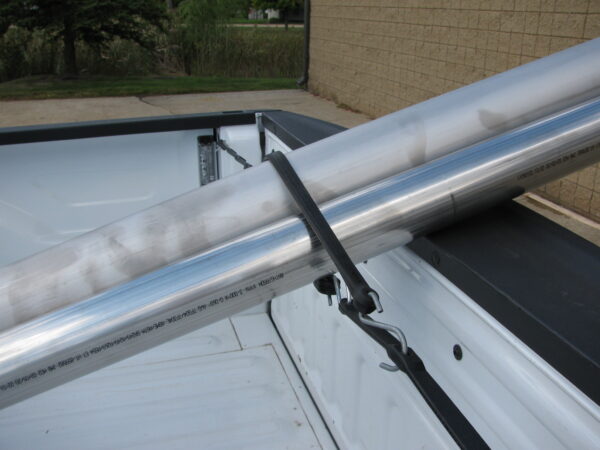 adjustable strap being used in the back of a pick up truck holding a pipe down