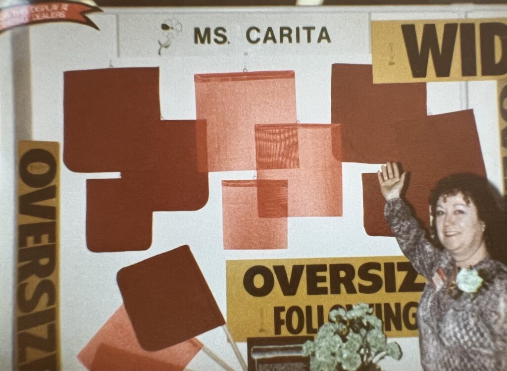 Carita 1980’s trucking tradeshow Ms. Carita herself at a truck show in front of truck safety signs and flags at a tradeshow