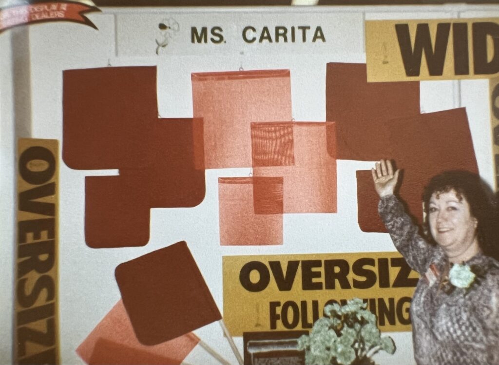 Ms. Carita herself at a truck show in front of truck safety signs and flags at a tradeshow