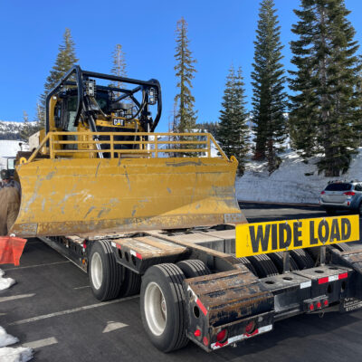Bulldozer on the back of a trailer with a WIDE LOAD Sign and Safety Flag