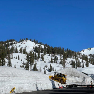 Bulldozer being unloaded off a trailer in a parking lot surrounded by snow